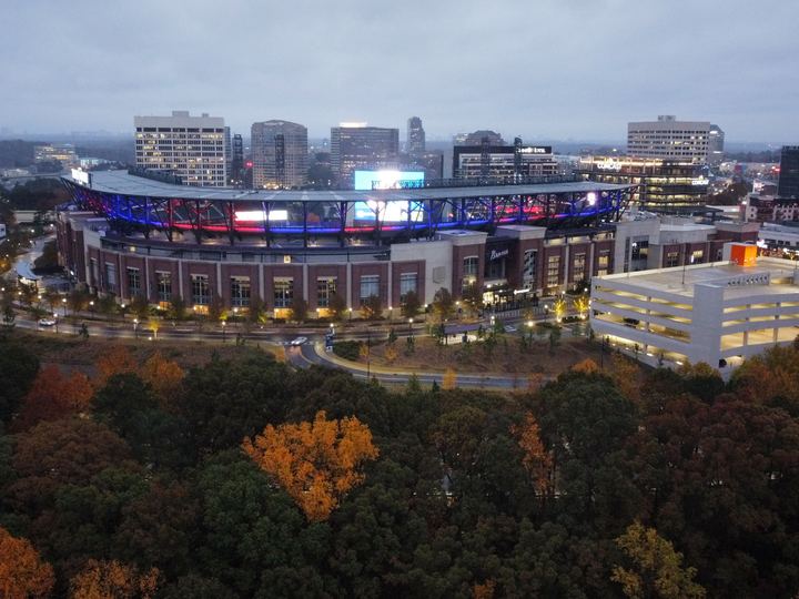 Truist Park lit up at dusk, seen from above with autumn trees in the foreground