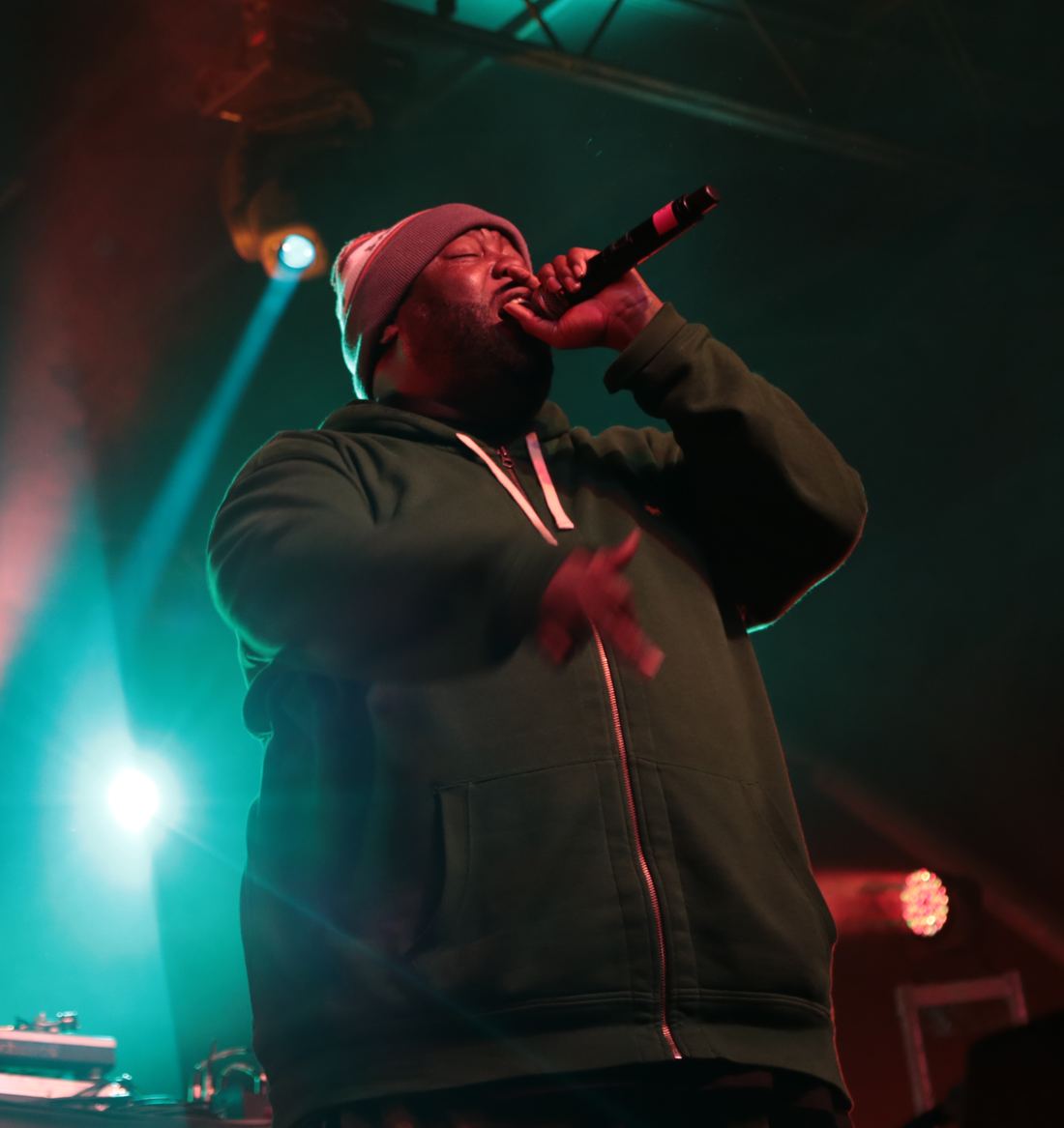 Killer Mike rapping into a microphone under green stage lights