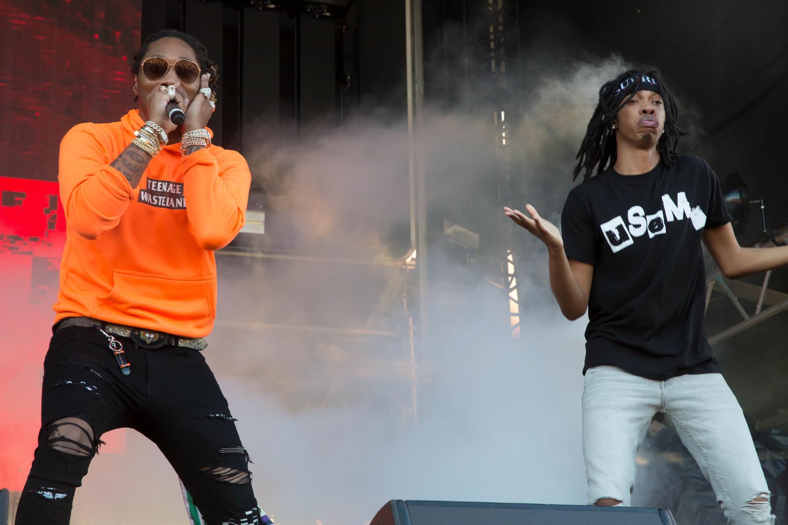 Atlanta rapper Future performing on an outdoor festival stage in an orange hoodie, with a hype man beside him in stage smoke