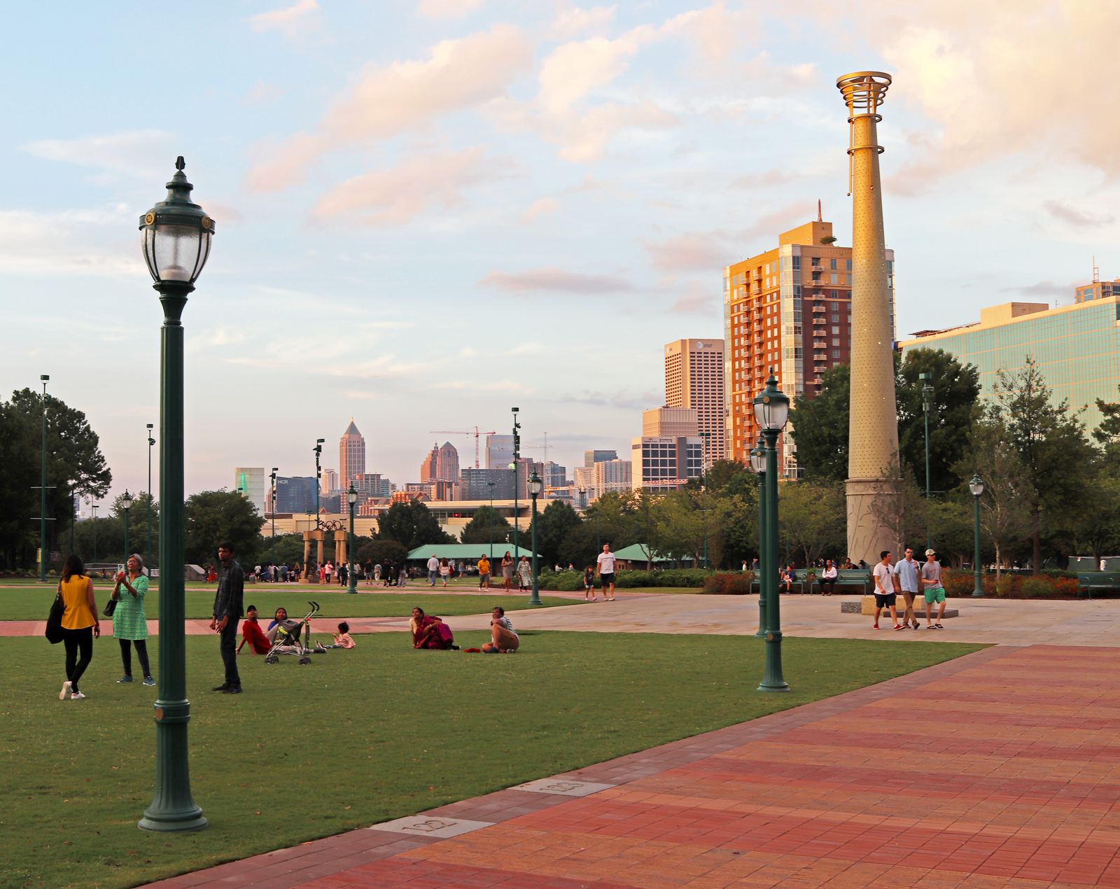 Lawn, lampposts and a tall commemorative column in Centennial Olympic Park at sunset