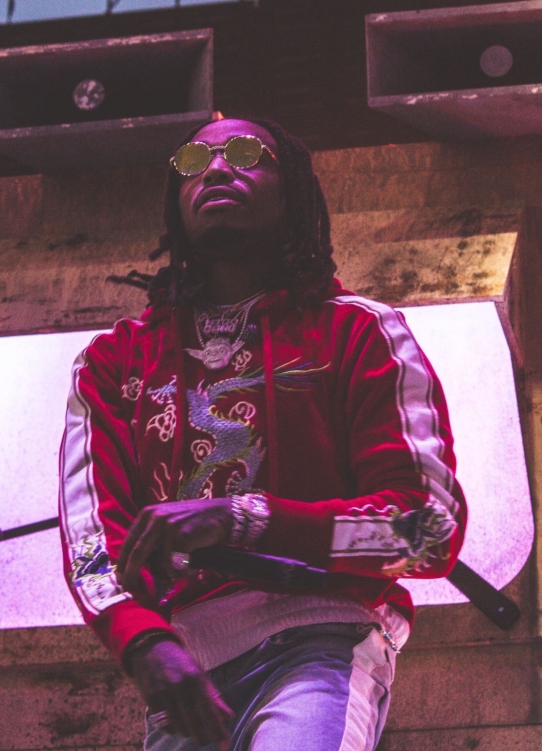 Quavo in a red jacket and sunglasses rapping into a microphone on stage