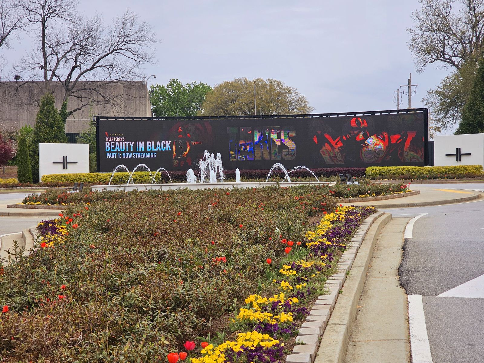 Landscaped entrance to Tyler Perry Studios with flower beds, fountains and a large display screen