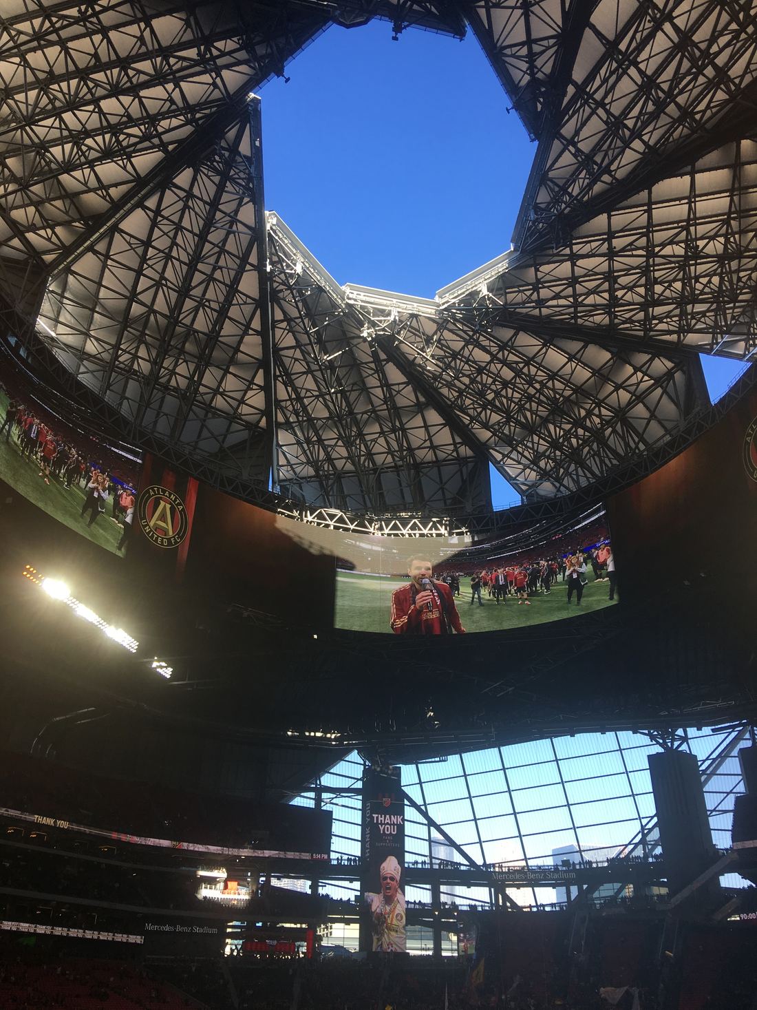 Looking up at the open pinwheel roof of Mercedes-Benz Stadium with blue sky visible